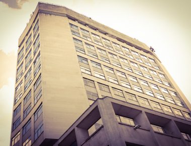 Tall, sepia-toned office building with numerous windows, viewed from a low angle against a cloudy sky.